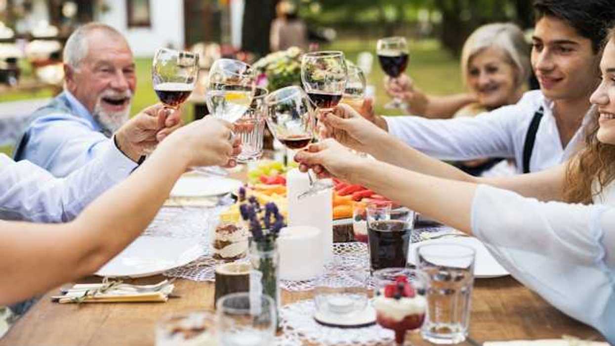 A group of people sitting at an outside table holding glasses of wine