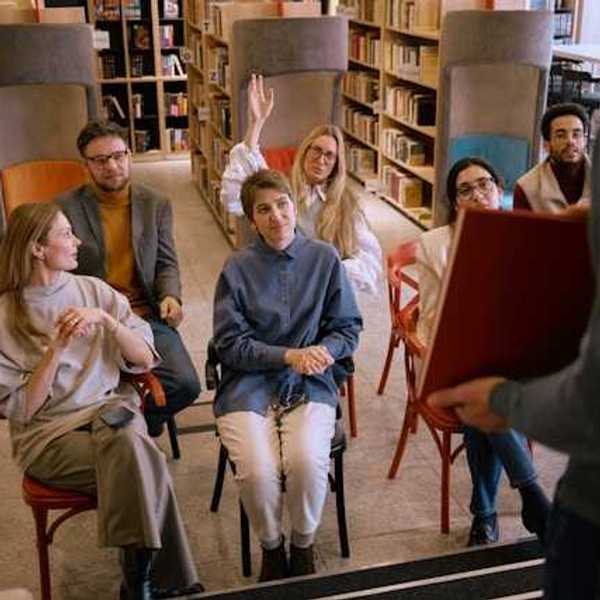 A group of people sitting in a library space listening to a speaker