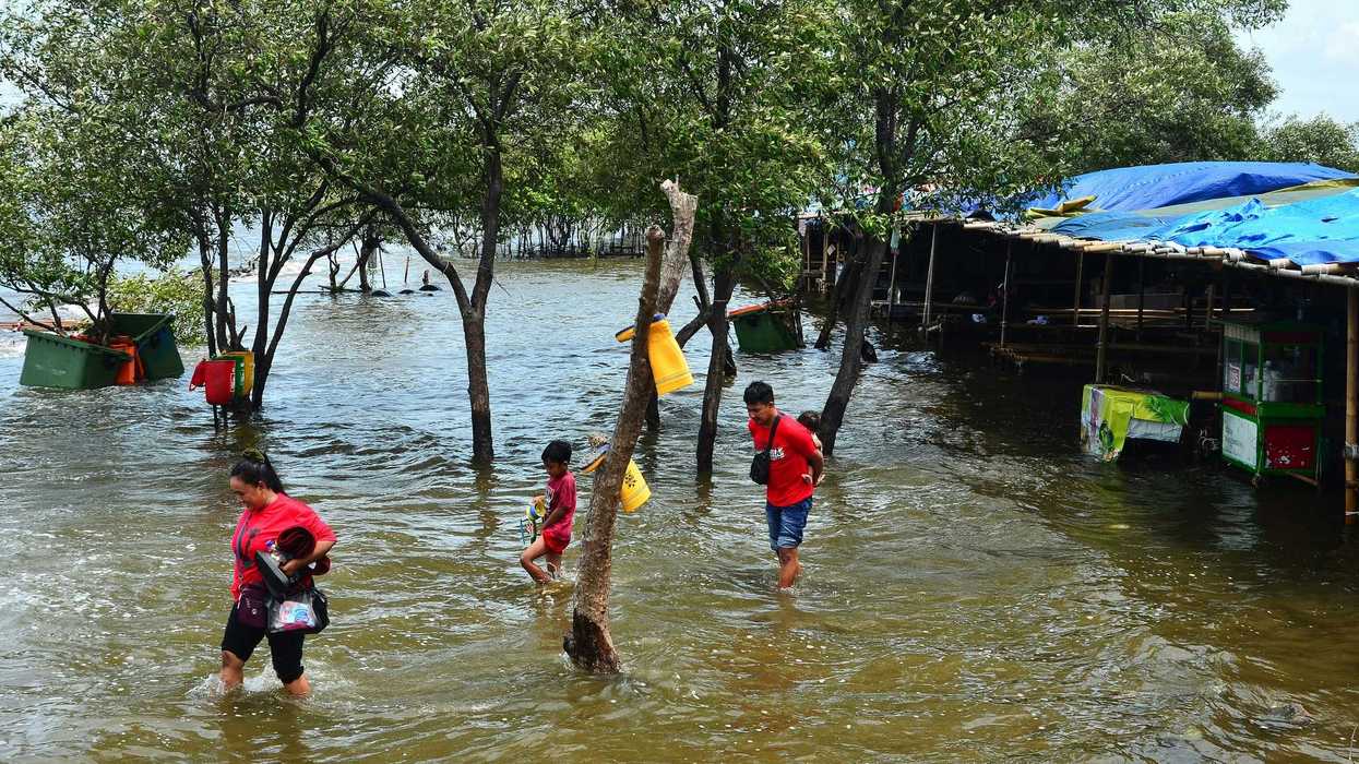 A group of people walking through a flooded street near the sea.