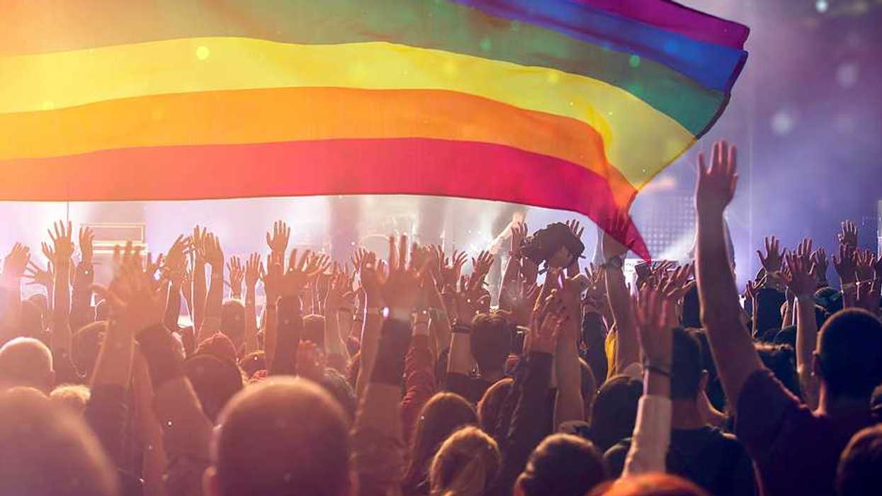 A group of people with their hands waving holding an LGBTQ flag in the air