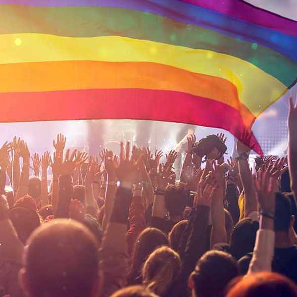 A group of people with their hands waving holding an LGBTQ flag in the air