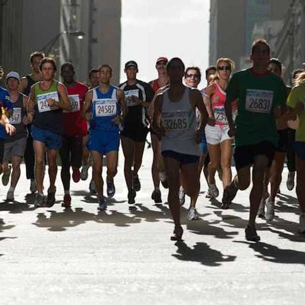 A group of runners with numbered tags running on a city street