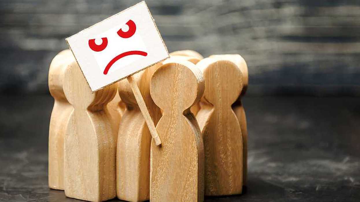A group of wooden figures shaped like people with a protest sign with a sad face on it