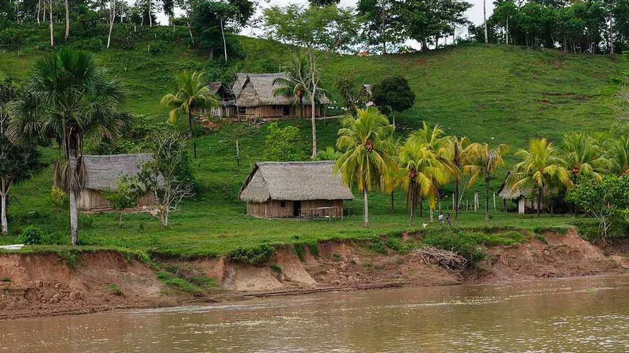 A group of wooden huts on a green hillside with a brown river running next to it