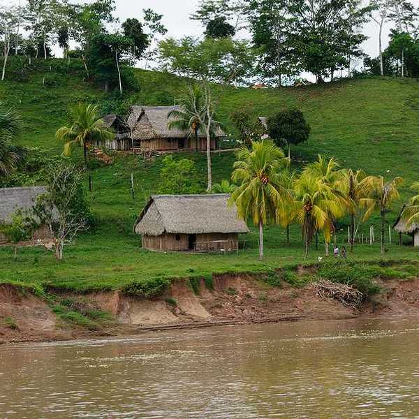 A group of wooden huts on a green hillside with a brown river running next to it