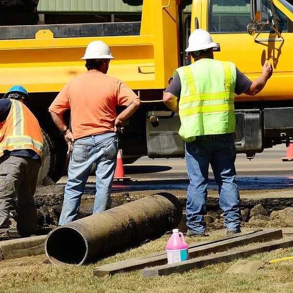 A group of workers standing next to a yellow truck fixing a pipe