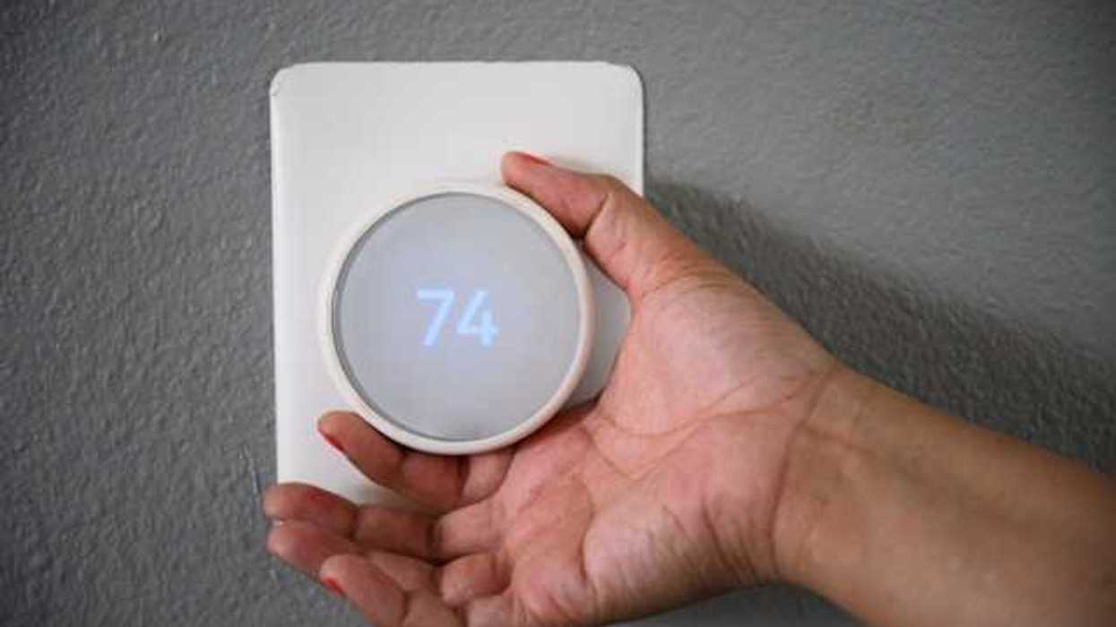 A hand adjusting the temperature on a wall thermostat