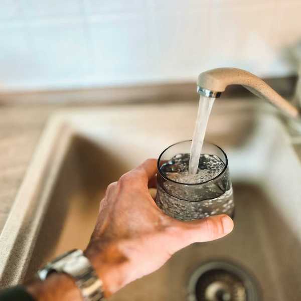 a hand holding a glass of water under running tap from sink.