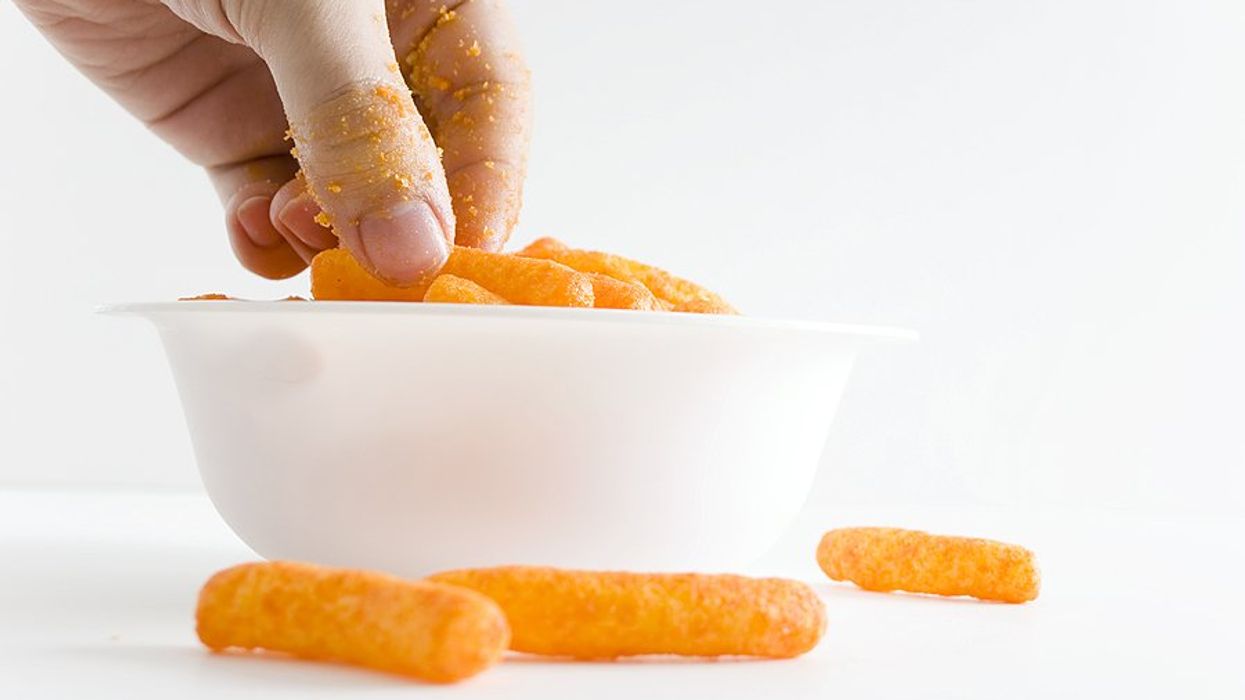 A hand reaching for cheese puffs in a white bowl