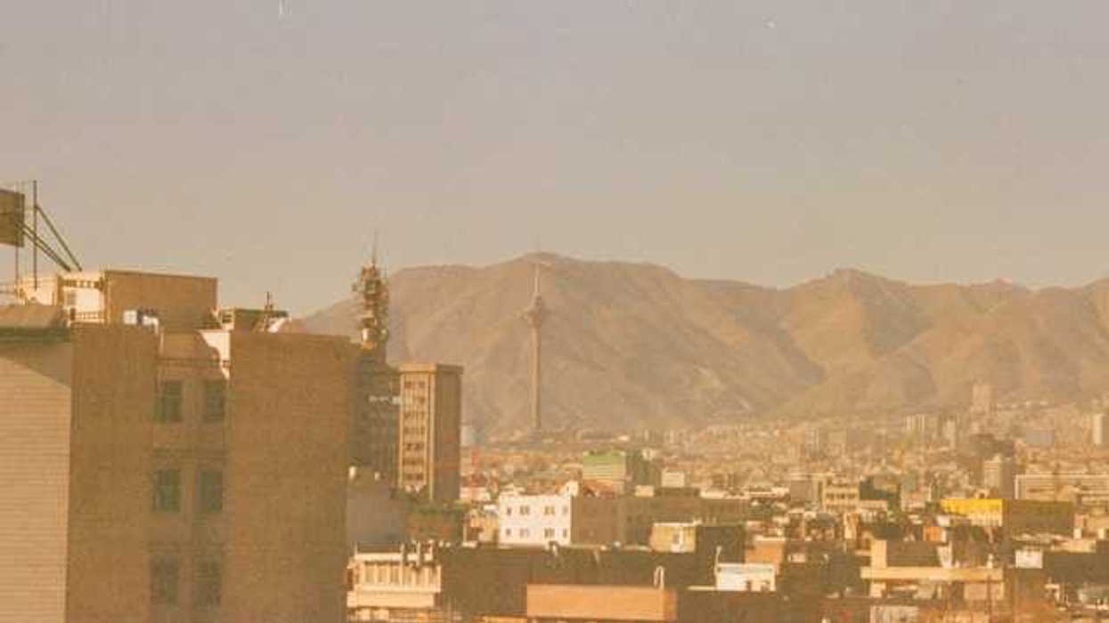 A hazy photo of the Tehran Province of Iran, with the Milad tower and mountains in the distance
