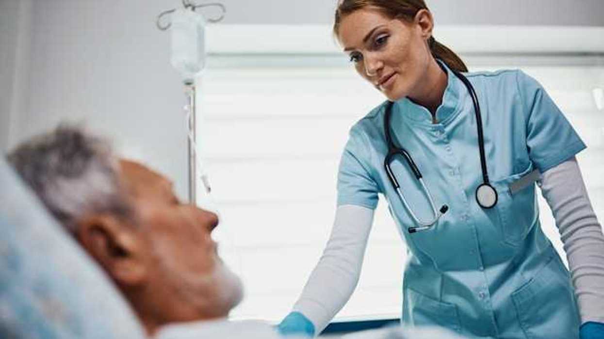 A health care professional wearing scrubs and a stethoscope leaning over an older patient in a bed