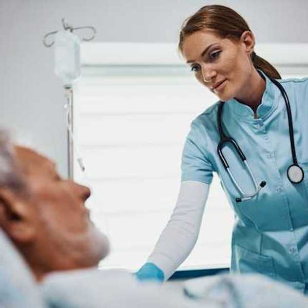 A health care professional wearing scrubs and a stethoscope leaning over an older patient in a bed