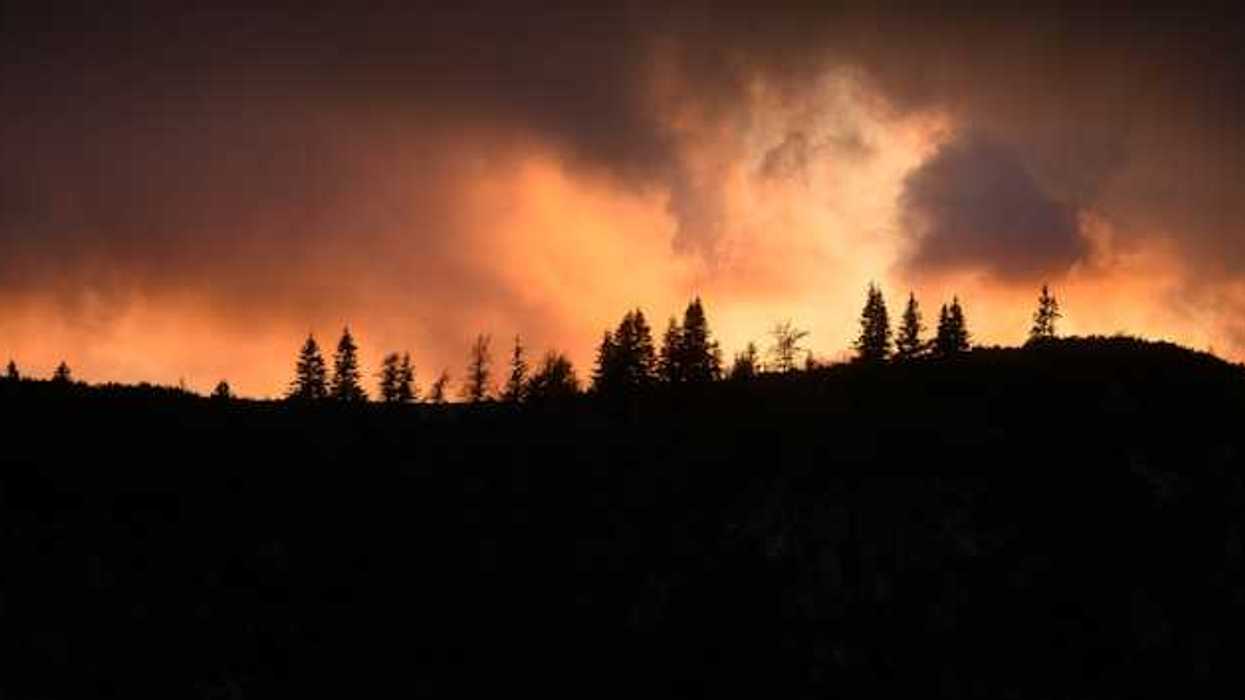 A hill silhouetted against a wildfire with smoke rising into the air