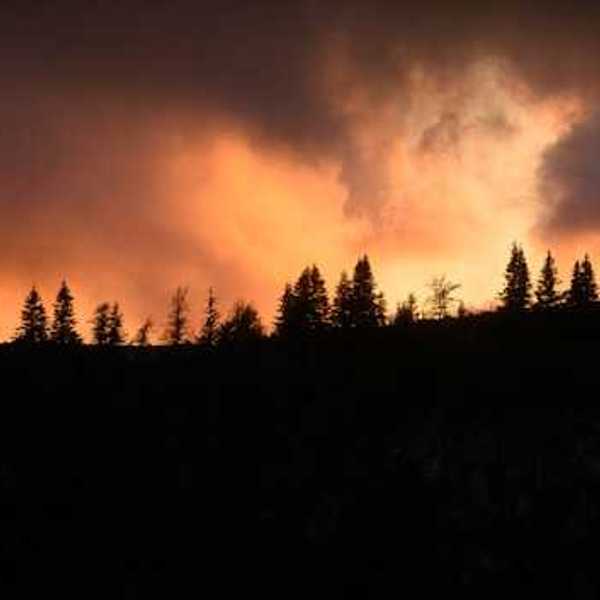 A hill silhouetted against a wildfire with smoke rising into the air