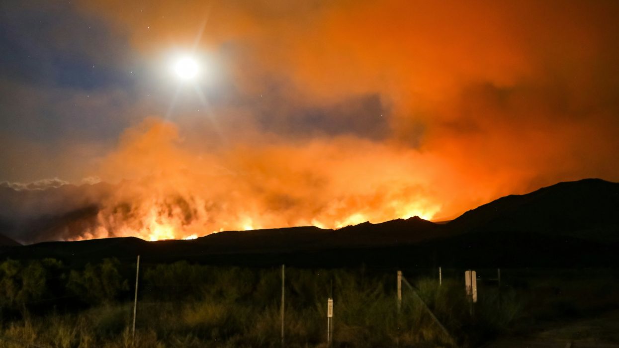 A hillside on fire with the moon in the background