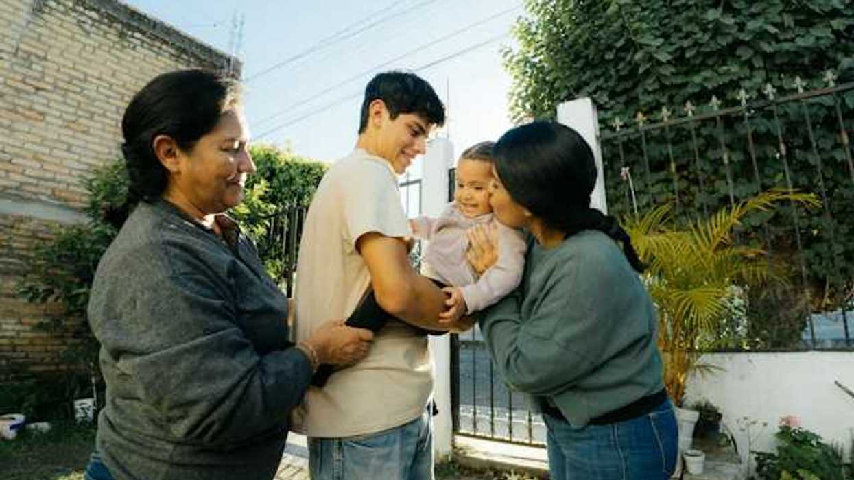 A hispanic family in their courtyard playing with a baby