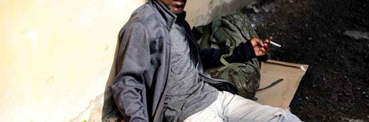 A homeless man sitting on the ground smoking a cigarette.