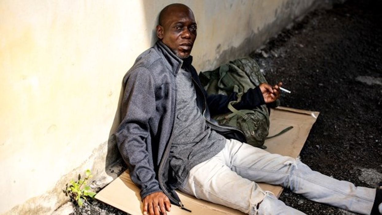 A homeless man sitting on the ground smoking a cigarette.