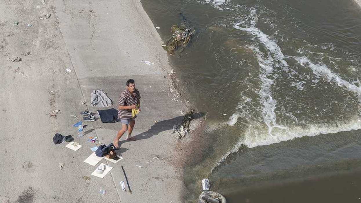 A homeless man with his belongings laid out on concrete river bank dries his clothes as he stands in his boxers and with a bandaged ankle along the heavily contaminated Tijuana River