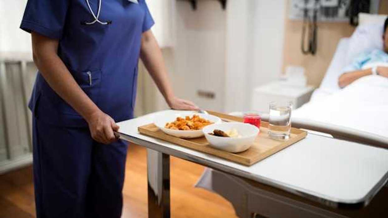 A hospital worker placing a tray of food on a tray for a hospitalized patient