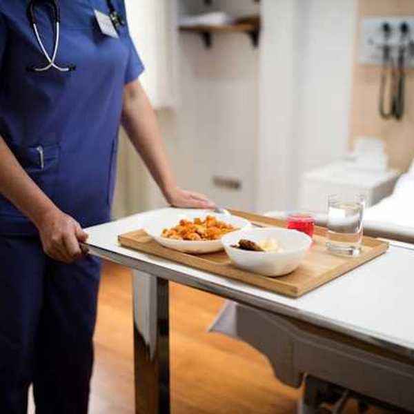 A hospital worker placing a tray of food on a tray for a hospitalized patient
