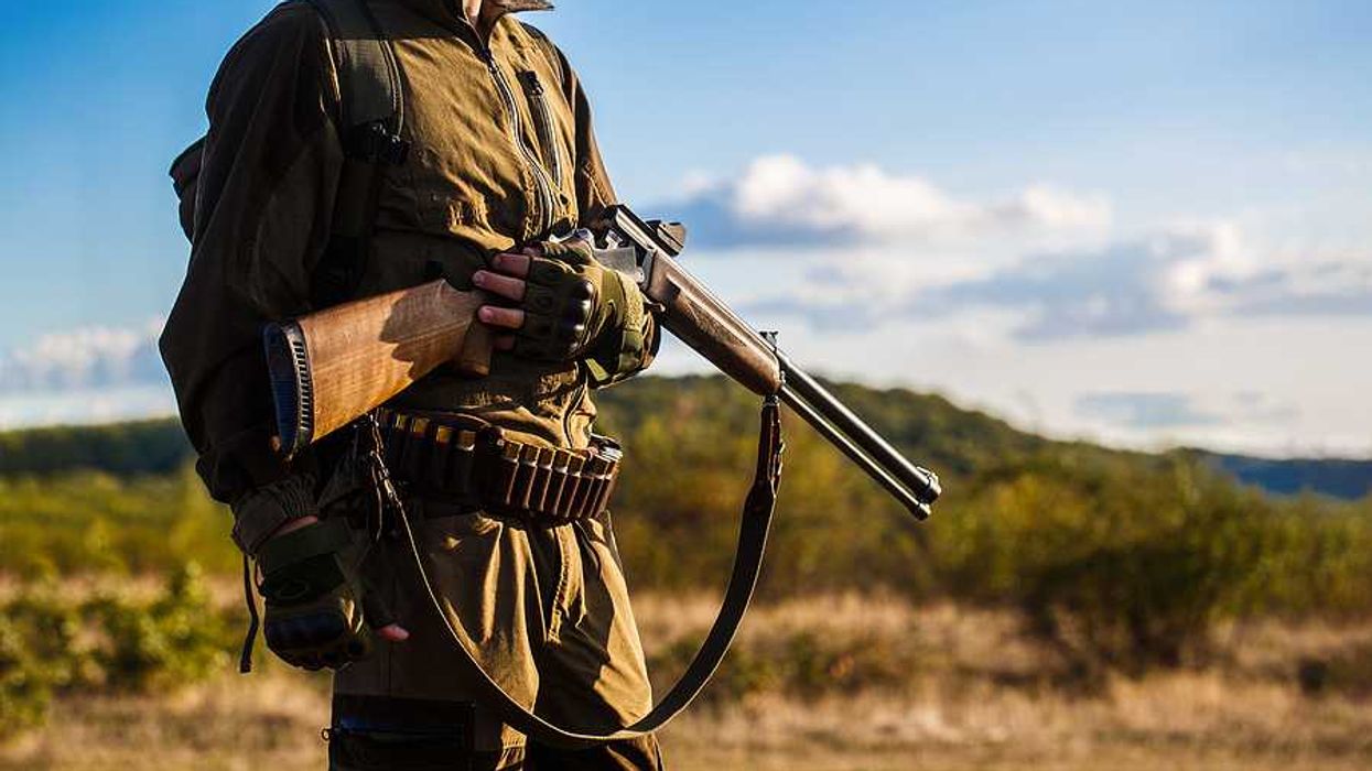 A hunter carrying a rifle in a wooded setting