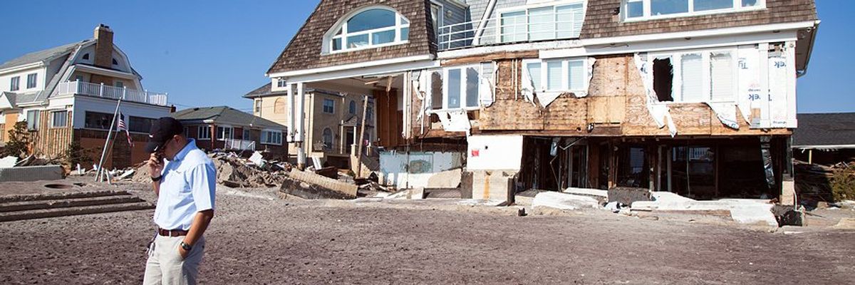 A hurricane damaged house with a man talking on the phone in front of it.