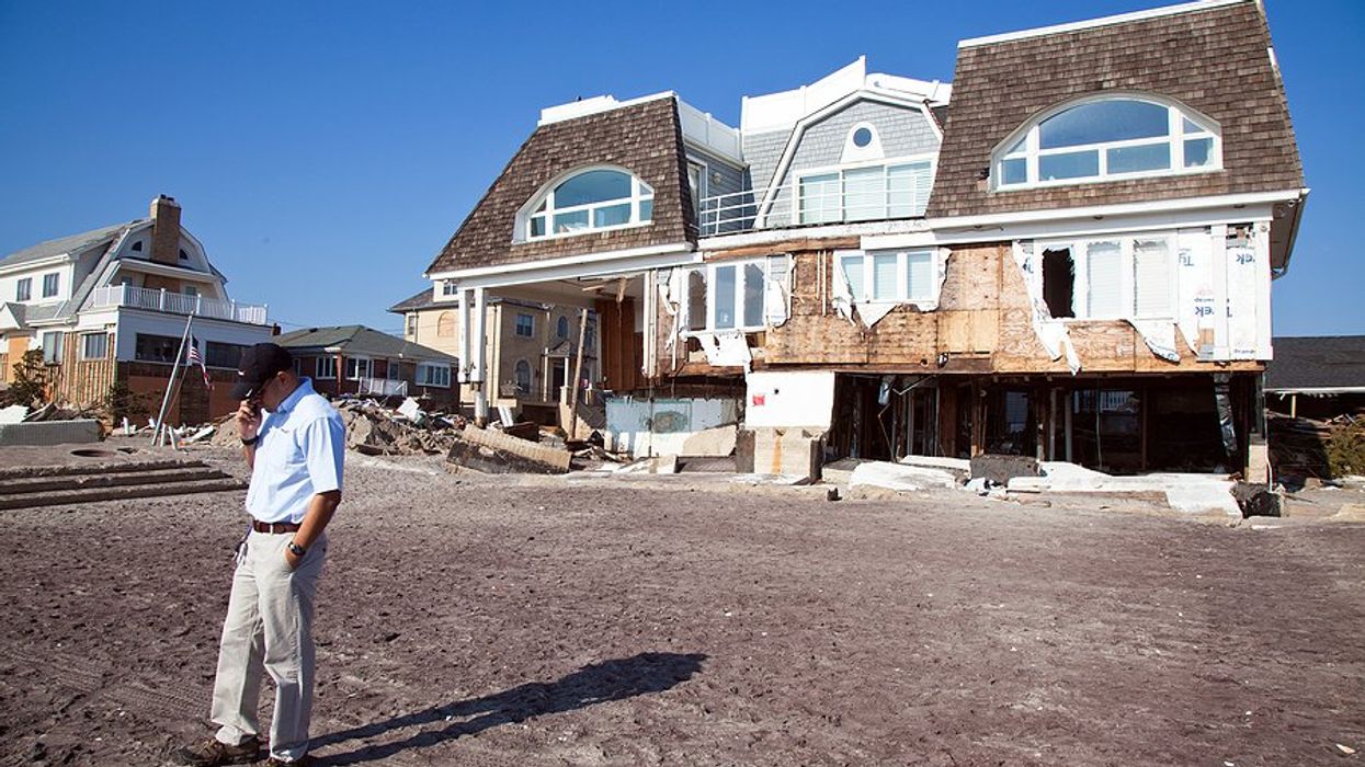 A hurricane damaged house with a man talking on the phone in front of it.
