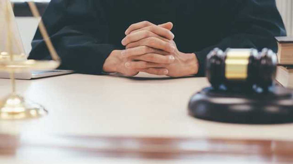 A judge with hands folded together and a gavel on their desk