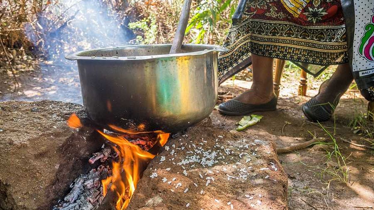 A kenyan woman cooking food in a large silver pot in the outdoors