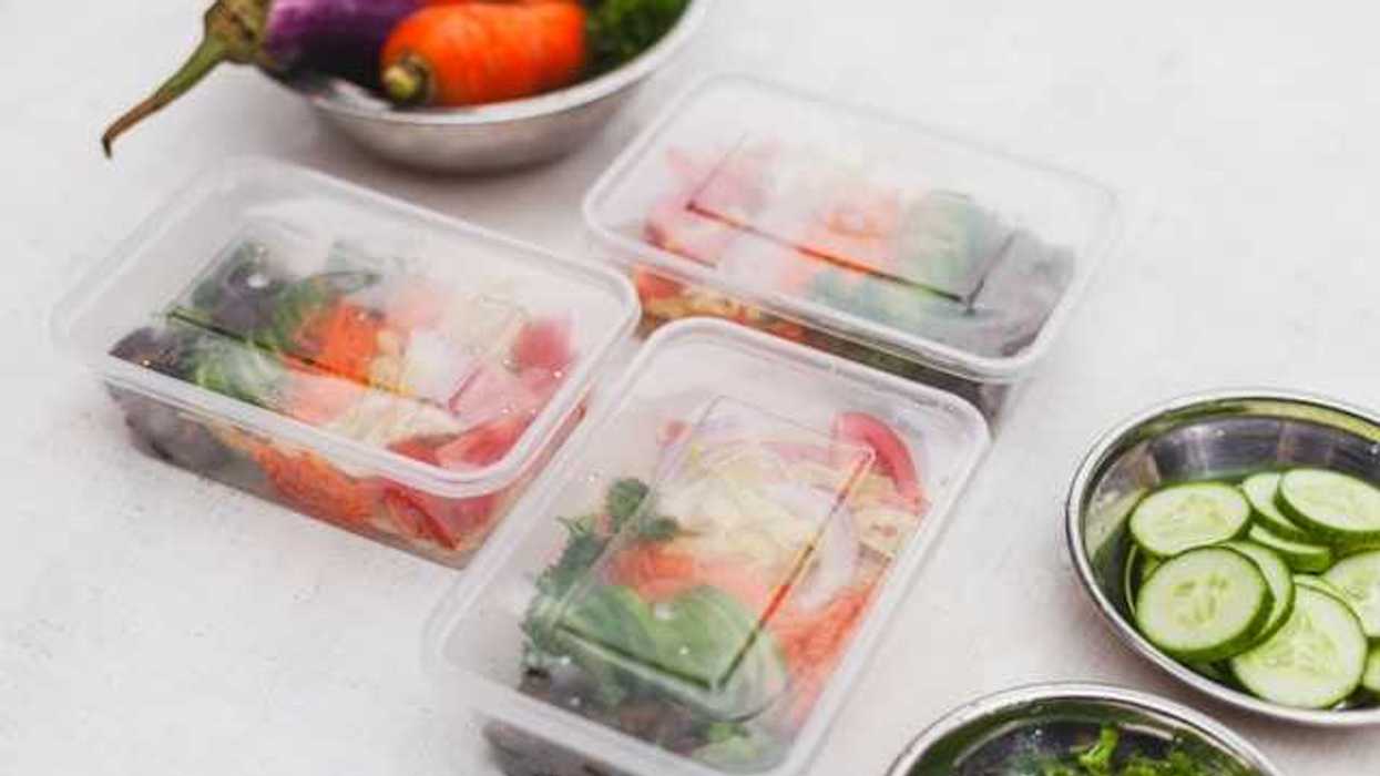 A kitchen counter with vegetables in silver bowls and packed food in plastic containers