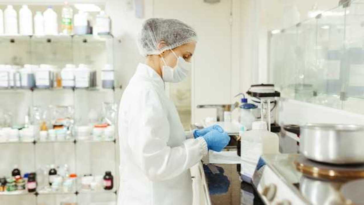 A lab technician wearing white coat and face mask working at a lab table