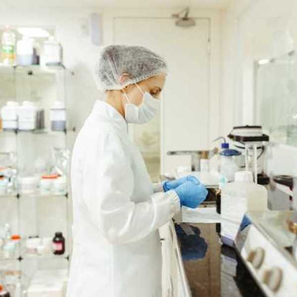 A lab technician wearing white coat and face mask working at a lab table