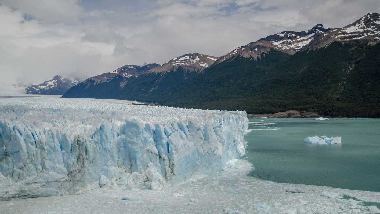 a large glacier and body of water with mountains in the background.