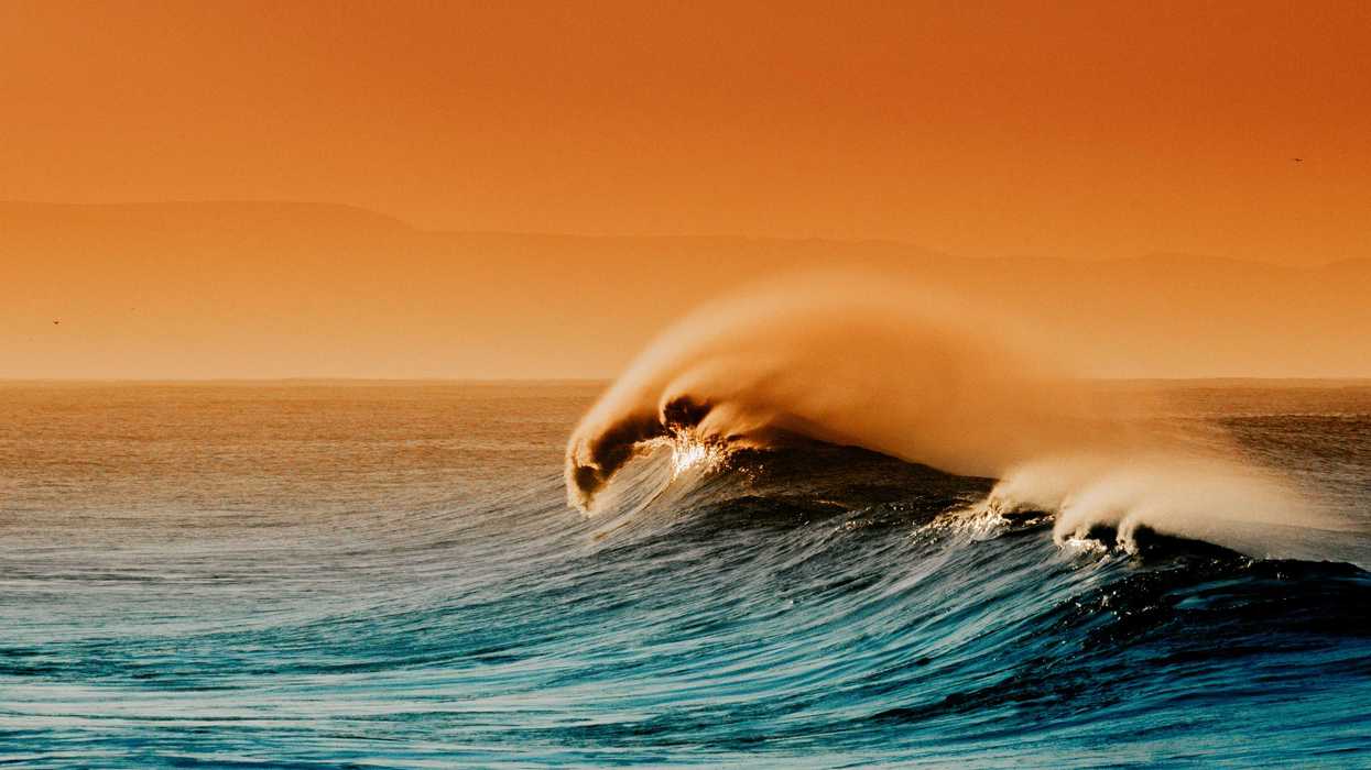 A large ocean wave breaks with an orange sky in background.
