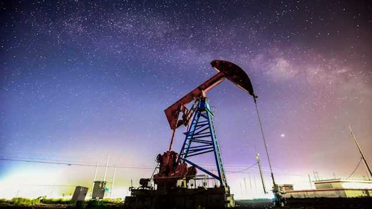 A large oil pump jack attached to the ground against a starry night sky background