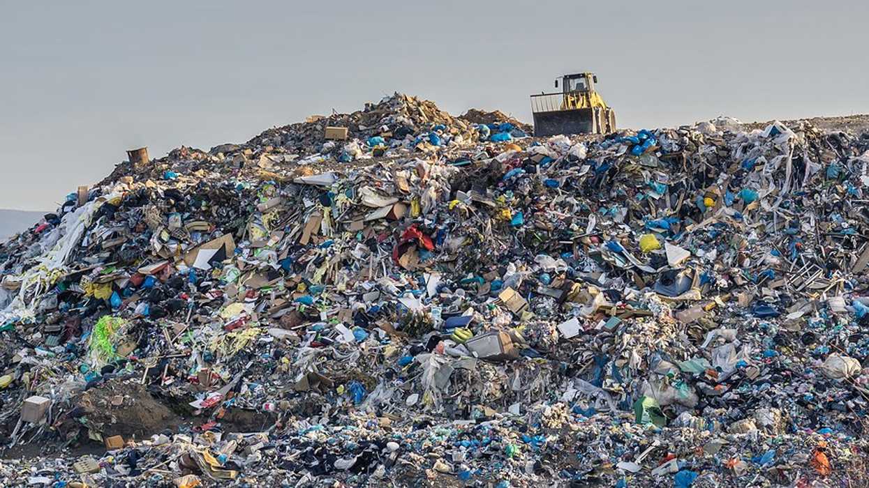 A large pile of waste in a landfill with a tractor perched at the top.