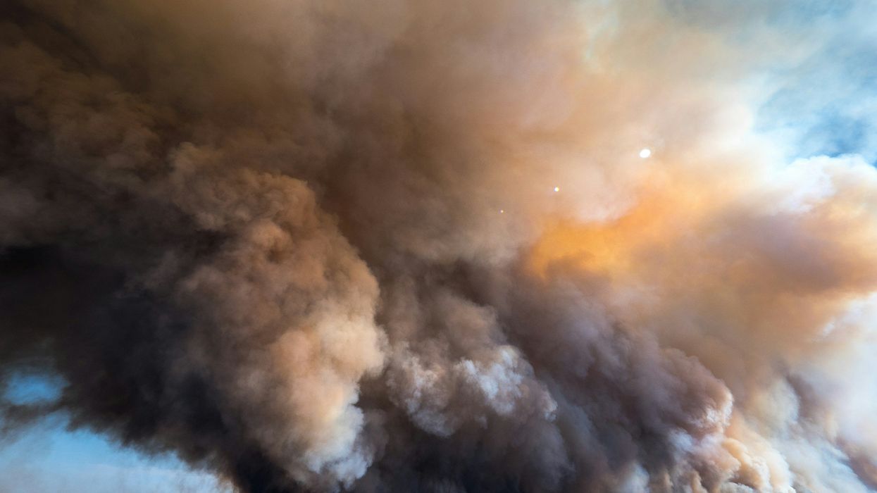 A large plume of smoke from a wildfire billows into the sky.