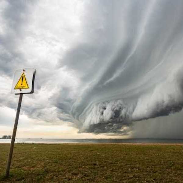 A large storm front approaching a beach from the ocean, with a danger sign in the foreground