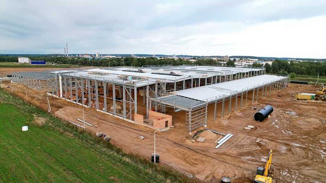A large warehouse under construction with green fields and a town in the distance