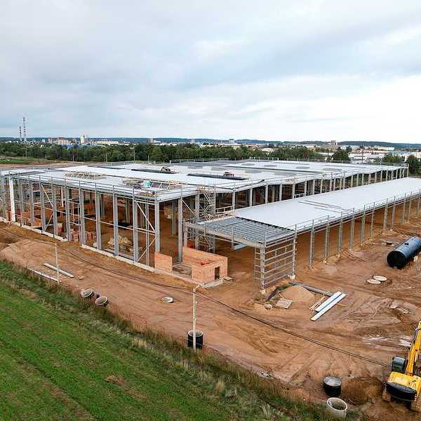 A large warehouse under construction with green fields and a town in the distance