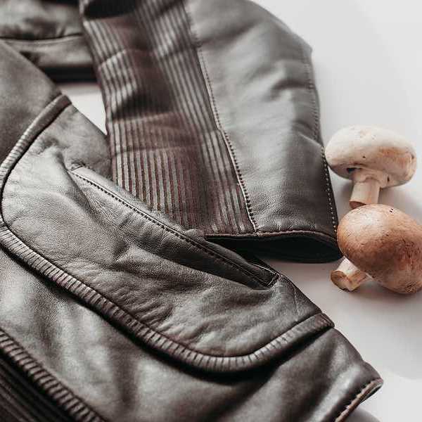 A leather jacket sitting next to three mushrooms on a white surface