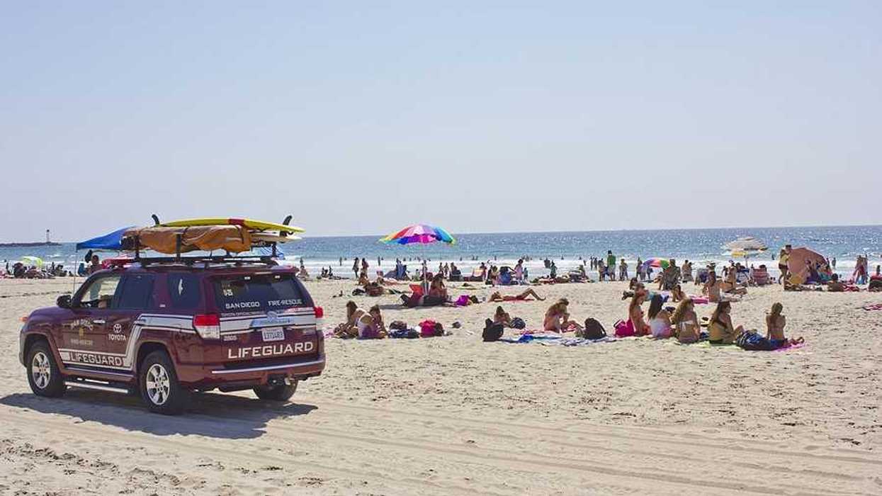 A lifeguard SUV on a beach with lots of people on it