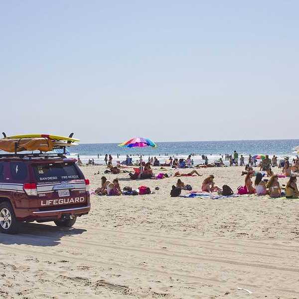 A lifeguard SUV on a beach with lots of people on it