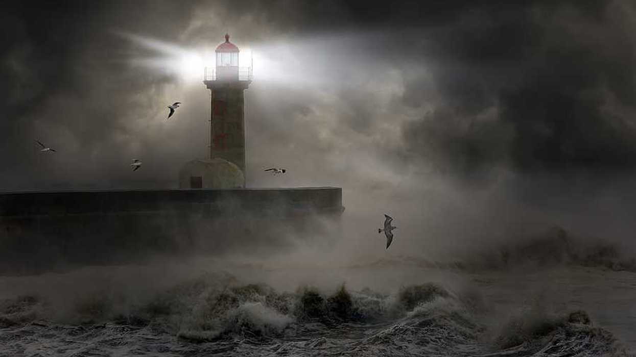 A lighthouse at the end of a promontory during a strong storm