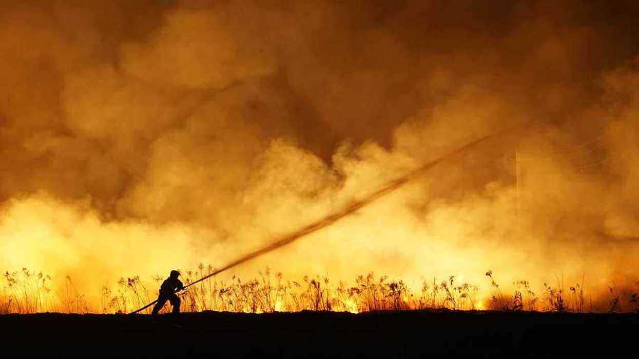 A lone firefighter training a stream of water on a huge wildfire