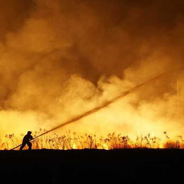 A lone firefighter training a stream of water on a huge wildfire