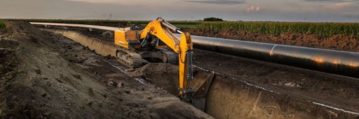 A machine digging a trench for a pipeline alongside an agricultural field.