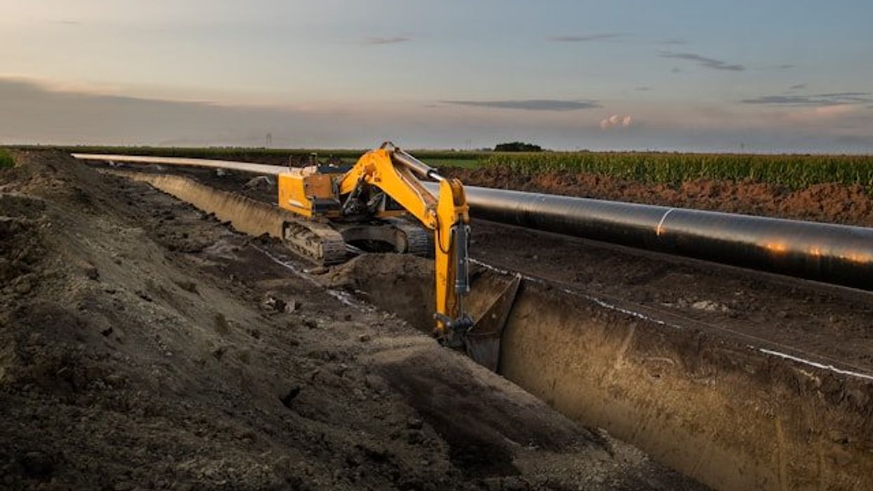 A machine digging a trench for a pipeline alongside an agricultural field.