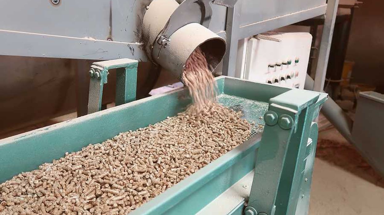 A machine dropping wood pellets into a green metal trough